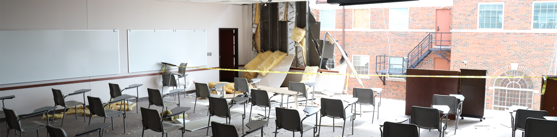 Classroom filled with desks facing a missing exterior wall.