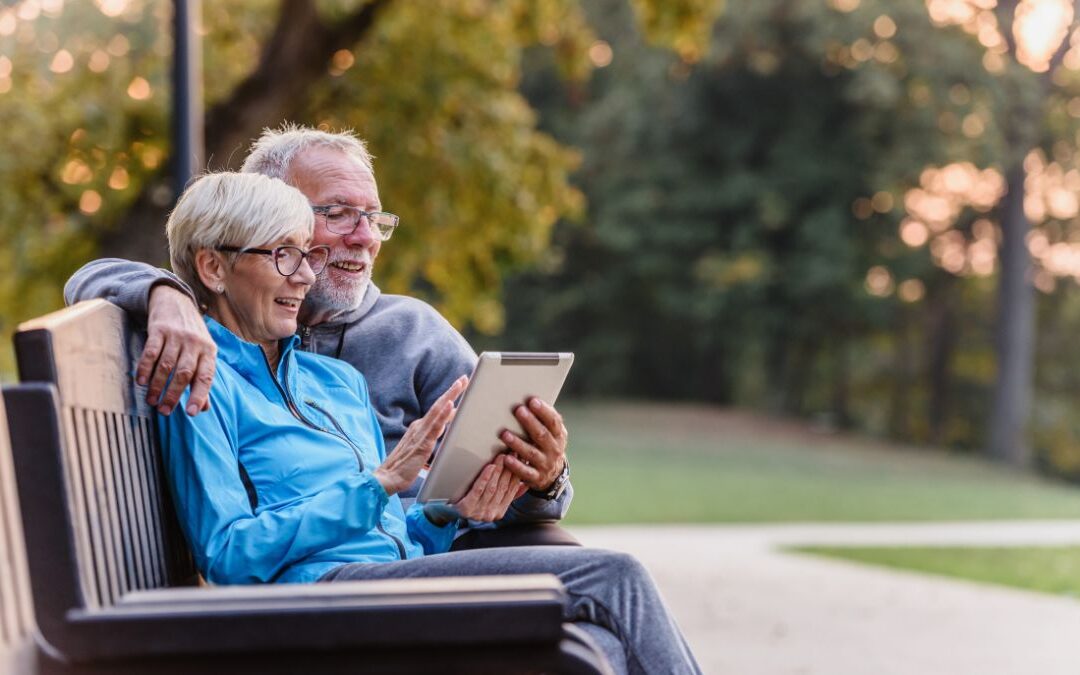 Smiling senior active couple sitting on the bench looking at tablet computer.